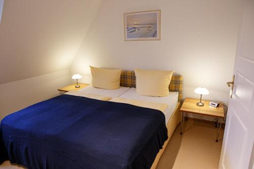 a small bedroom with a blue bed and two tables at Friesennest in Oldsum