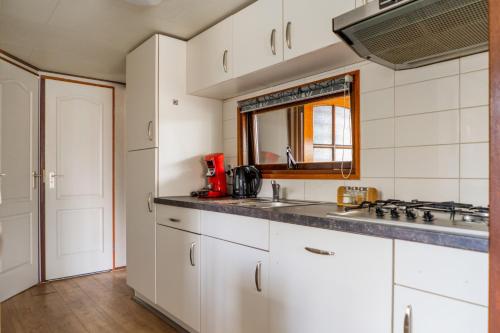 cocina con armarios blancos, lavabo y espejo en Drents Genieten - Struikheide met privé whirlpool, en Erm