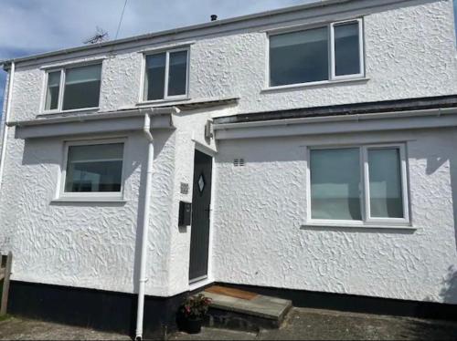 a white house with a black door and windows at Isle of Anglesey Spacious Home in Llanfairpwllgwyngyll