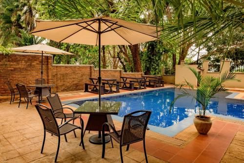 a table and chairs with an umbrella next to a pool at Serendib Suites and Conference Center in Blantyre
