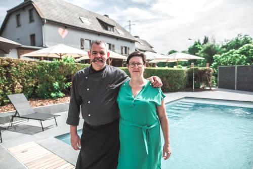 a man and a woman standing next to a swimming pool at Hotel Au Coeur de Lacuisine in Florenville