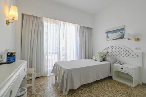 a white bedroom with a bed and a window at Hotel Pinos Playa in Cala Santanyi