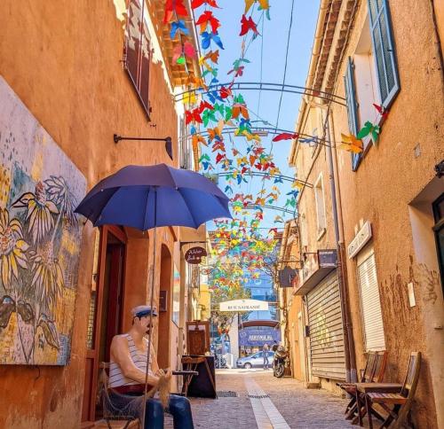 un homme assis sous un parapluie dans une rue dans l'établissement BOULOURIS - Grand 3 pièces 5 personnes avec terrasse à 5min à pied des plages, à Saint-Raphaël