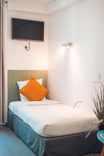 a bed with an orange pillow and a tv on the wall at Logis Hôtel Vuillot in Cuiseaux