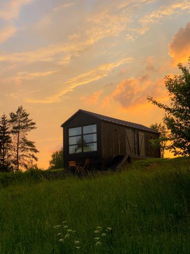 eine kleine Hütte auf einem Feld mit Sonnenuntergang im Hintergrund in der Unterkunft Ragnar Glamp Milzkalne Lux in Rauda