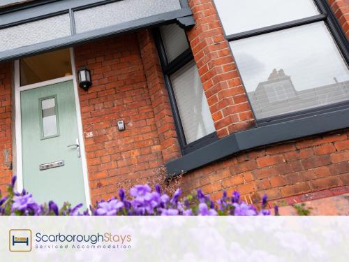 a brick house with a green door and purple flowers at Scarborough Stays - Ashville Lodge - 5 Bedroomed house - Sleeps 9 in Scarborough