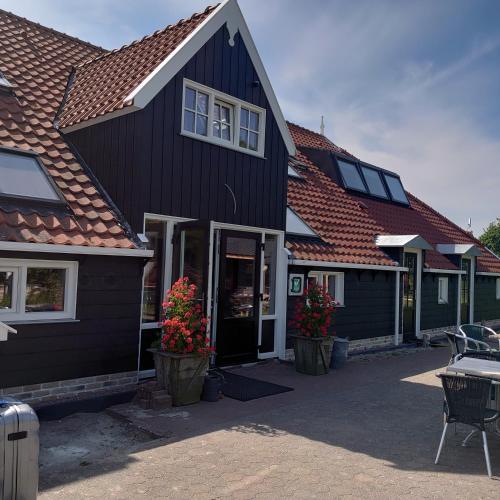 a black house with red roofs and flowers in pots at De Cyprian Bed & Breakfast in Baaiduinen