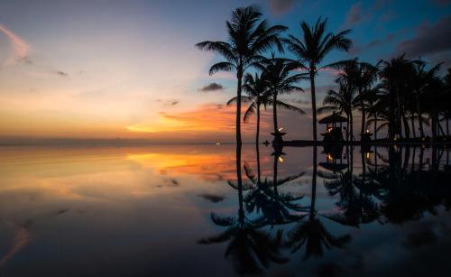 a pool with palm trees and the ocean at sunset at The Legian Seminyak, Bali in Seminyak