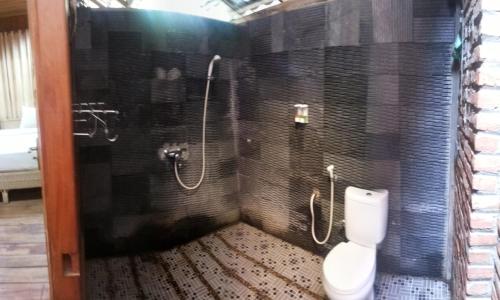 uma casa de banho com um WC e um chuveiro com azulejos pretos em Jazz Hotel Palu em Palu