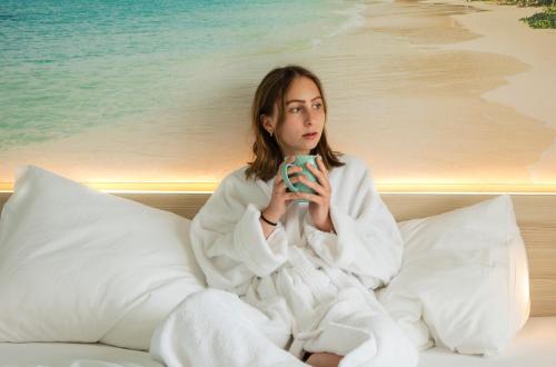 a woman sitting on a bed holding a cup of coffee at Hi5-Hotel Seiersberg in Windorf