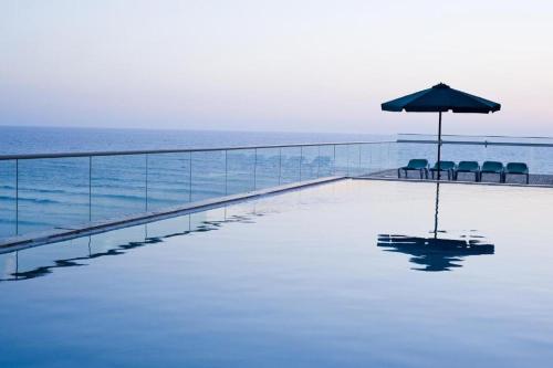 a swimming pool with an umbrella and chairs and the ocean at Share Suites Hotel Bat-Yam in Bat Yam