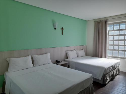 2 Betten in einem Zimmer mit einem Kreuz an der Wand in der Unterkunft CEIC Pousada e Eventos in Nova Trento