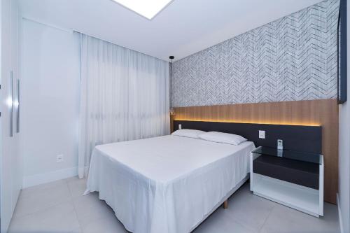 ein Schlafzimmer mit einem weißen Bett und einer Wand in der Unterkunft Adra 102 - Apartamento no centro de Bombinhas - Finamente mobiliado e decorado - Rooftop com piscina e academia - À poucos metros da praia in Bombinhas