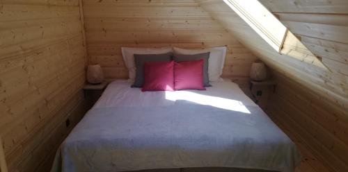 a bed with two pink pillows in a wooden room at Woodorf drewnem usłane - domki z bala nad rzeką Słupią wśród pól i lasów z chatą grillową, ogniskiem i placami zabaw dla dzieci -Royal Red House z jacuzzi i ogrodzonym extra ogródkiem dla piesków, Royal Green House - bez jacuzzi in Ustka