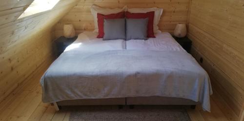 a bedroom with a bed with white sheets and red pillows at Woodorf drewnem usłane - domki z bala nad rzeką Słupią wśród pól i lasów z chatą grillową, ogniskiem i placami zabaw dla dzieci -Royal Red House z jacuzzi i ogrodzonym extra ogródkiem dla piesków, Royal Green House - bez jacuzzi in Ustka