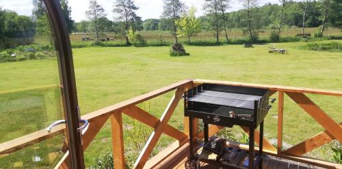 a grill on a deck with a field of grass at Woodorf drewnem usłane - domki z bala nad rzeką Słupią wśród pól i lasów z chatą grillową, ogniskiem i placami zabaw dla dzieci -Royal Red House z jacuzzi i ogrodzonym extra ogródkiem dla piesków, Royal Green House - bez jacuzzi in Ustka