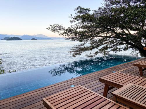 a wooden deck with a swimming pool next to the water at Casa Luz in Paraty