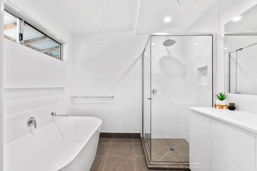 a white bathroom with a tub and a glass shower at 7 Depper Cosy Beach House in Central Sunshine Beach in Sunshine Beach