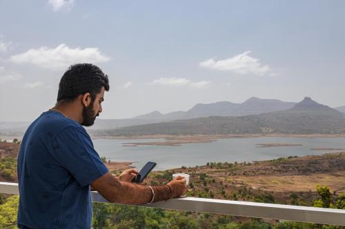 a man holding a cell phone and a cup of coffee at SaffronStays Ahilya Waters by Kosha Villas, Pawna - pool villa with panoramic view of Pawna Lake in Āmbavna
