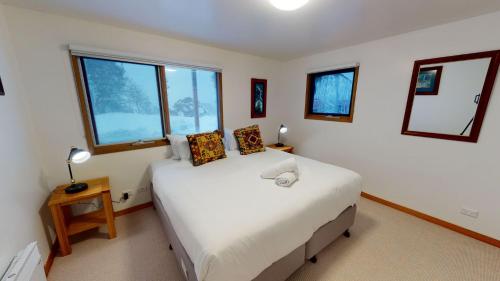 a bedroom with a large white bed with windows at Family Chalet 35 - The Stables Perisher in Perisher Valley