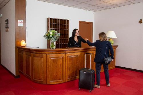a woman is standing at a reception desk at Hôtel L'Ours De Mutzig in Mutzig