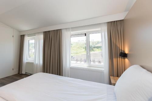 a bedroom with a white bed and windows at Centrum-Appartementen Langstraat 5 in Zoutelande