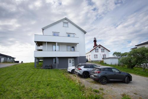 twee auto's geparkeerd voor een witte huis met een vuurtoren bij Apt 202 - Andenes Whale Safari Apartments in Andenes