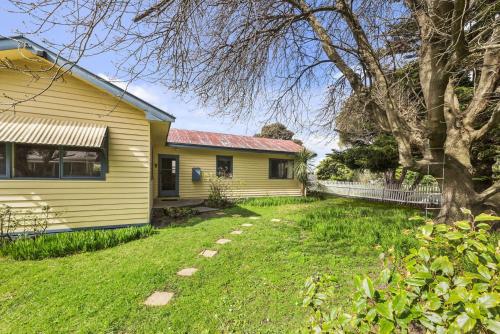 a yellow house with a tree and a yard at Oak And Pine in Apollo Bay
