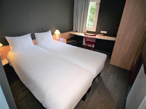 a large white bed in a room with a desk at ibis Nemours in Nemours