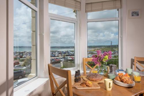 a dining room with a table with food and a window at Cormorant Views, Marazion in Marazion
