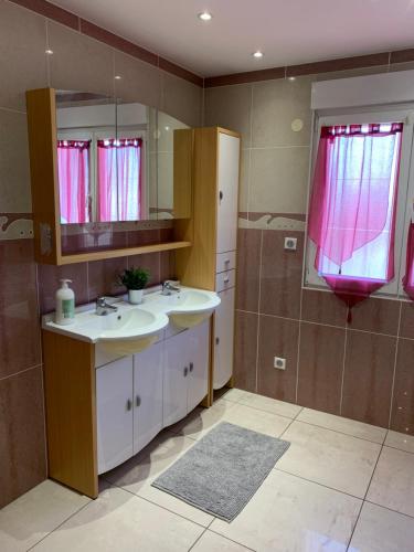 uma casa de banho com 2 lavatórios, um espelho e cortinas cor-de-rosa em La terrasse du parc em Marckolsheim