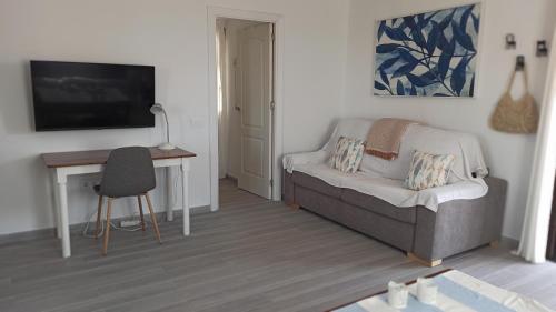 ein Wohnzimmer mit einem Sofa und einem Schreibtisch mit einem TV in der Unterkunft Lomas del Castillo, la casa de la isla in Caleta de Fuste