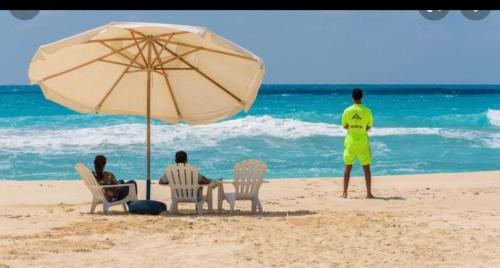 two people sitting in chairs under an umbrella on the beach at North coast sedra resort villa قريه سيدرا الساحل الشمالي in Alexandria