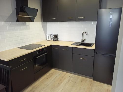 a kitchen with black cabinets and a sink and a refrigerator at Apartament Letnicka, Nowy, 950m od morza in Gdańsk
