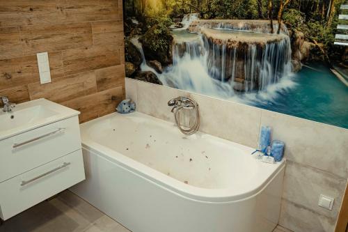 a bathroom with a tub and a waterfall painting on the wall at Domki Nadmorski Relax in Jastrzębia Góra