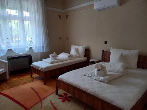 una camera con due letti con lenzuola bianche e un peluche sopra di Szent István Wellness Panzió a Makó
