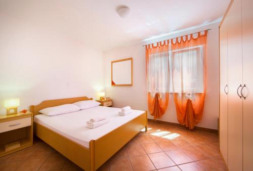 Schlafzimmer mit einem Bett mit weißer Bettwäsche und orangefarbenen Vorhängen in der Unterkunft Apartments Villa Dorida in Komarna