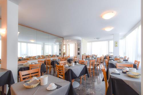 un comedor con mesas, sillas y ventanas en Hotel Janeiro, en Caorle