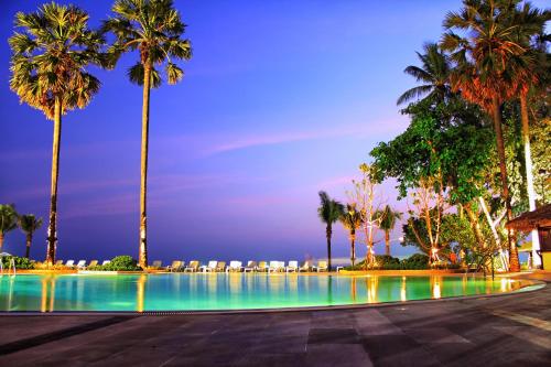 a swimming pool with palm trees and chairs at night at Novotel Rayong Rim Pae Resort in Klaeng