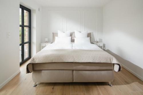 a white bedroom with a large bed and two windows at Küsten Suite Nord - direkte Wasserlage, Terrasse, 70qm in Greetsiel