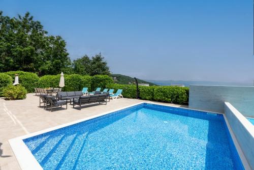 a swimming pool with chairs and a table next to at Villa Sveti Petar - with heated pool and outdoor jacuzzi in Opatija