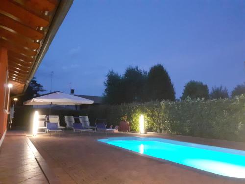 uma piscina à noite com cadeiras e um guarda-sol em B&B Casa di Chiara em San Michele al Tagliamento