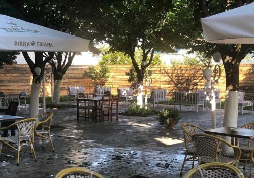 un patio al aire libre con mesas, sillas y árboles en Hotel Xhelili, en Cërrik