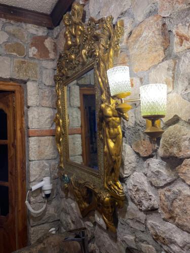 a gold mirror on a stone wall with a lamp at Solomon&Sons in Dhërmi