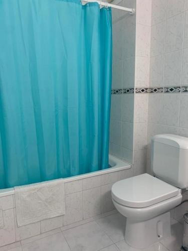 a bathroom with a toilet and a blue shower curtain at Apartamento T1 Monte Gordo in Monte Gordo
