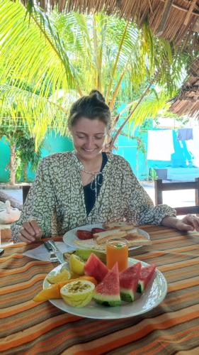 a woman sitting at a table with a plate of fruit at HOMELAND SWAHILI LODGE Nungwi Backpacker Apartments BUDGET in Nungwi