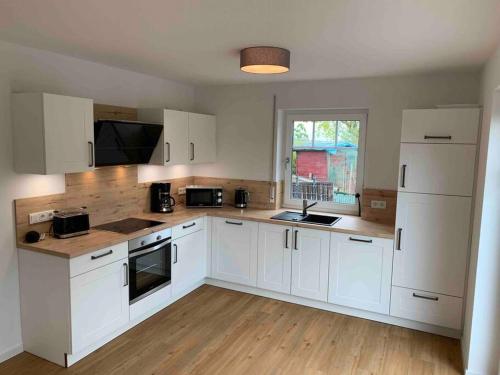 a kitchen with white cabinets and a wooden floor at Ferienhaus Meerzeit in Krummhörn