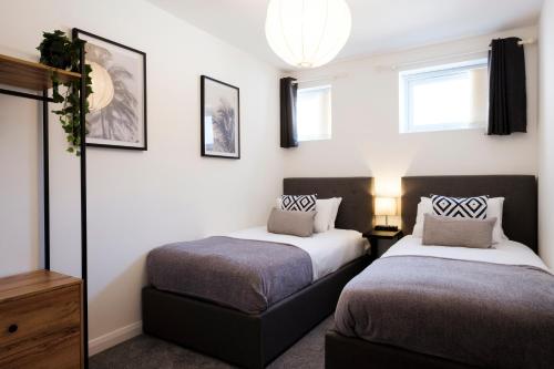 Duas camas num quarto com paredes brancas e janelas em Corinium Lodge - town centre apartment em Cirencester