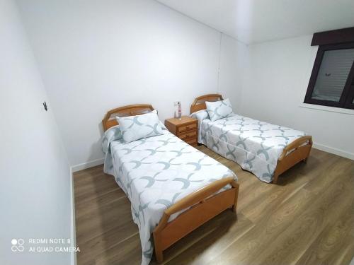 Habitación con 2 camas, paredes blancas y suelo de madera. en Villa Lupita, en Sanxenxo