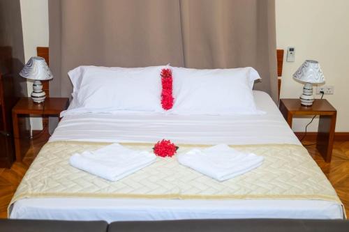 a white bed with two towels and a red flower on it at Will's Sea View Apartments in Victoria